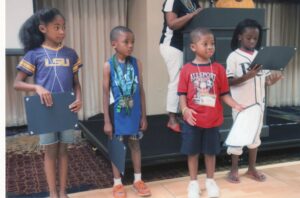 During the banquet, at the Neal Family Reunion, certificates were presented to Young Family Achievers. Certificates for several age groups recognized individual accomplishments also chronicled in the family reunion booklet. Here “Seedling Awards” are given to the youngest group (left to right) Lillian Nabors (6), Ethan Parrish (5), Amaris Johnson (5), and Karys Rhodan (7). Members wore favorite team shirts for the banquet.