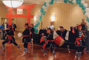 Kubasaki High School was located on Okinawa. For a “Brat” reunion (“children” of military personnel) in Fairfax County, Virginia, reunion planners decorated their Hospitality Room with a Japanese theme and colors. They made a large cardboard tori (ceremonial gate outside Shinto temples), painted it red and it was the centerpiece for the Hospitality Room.Here a Japanese drum troop entertains.